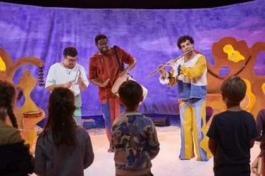 Drei Musiker spielen Flöte und Percussion vor einer Gruppe von Kindern.