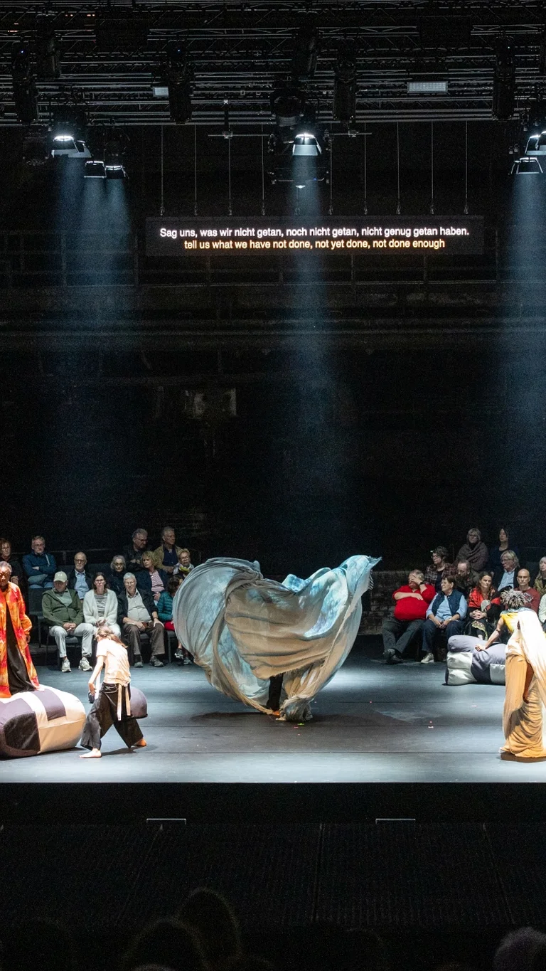 Stage with performers and musicians, with audience sitting in the background.
