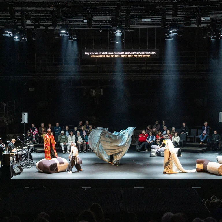 Stage with performers and musicians, with audience sitting in the background.