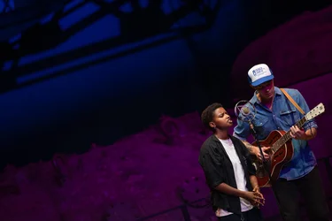 Meskerem Mees und Carlos Garbin musizieren gemeinsam vor einer pink beleuchteten Industriemaschine.
