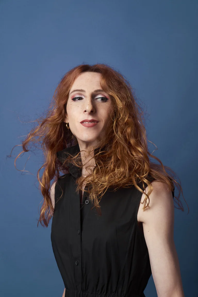 Nina Laisné stands in front of a blue background. She is wearing a black sleeveless dress with a stand-up collar.