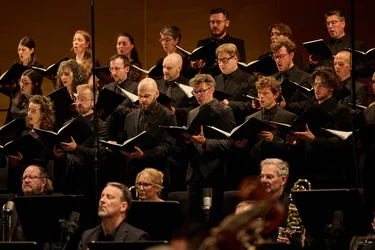 Chorwerk Ruhr singt mit geöffneten Notenmappen, begleitet von den Bochumer Symphonikern.