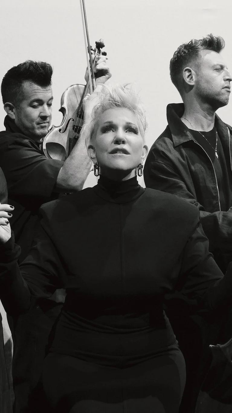 Schwarz-weiß-Aufnahme von Joyce DiDonato, die von den drei Musiker:innen von Time for Three umgeben ist, die auf ihren Streichinstrumenten spielen.
