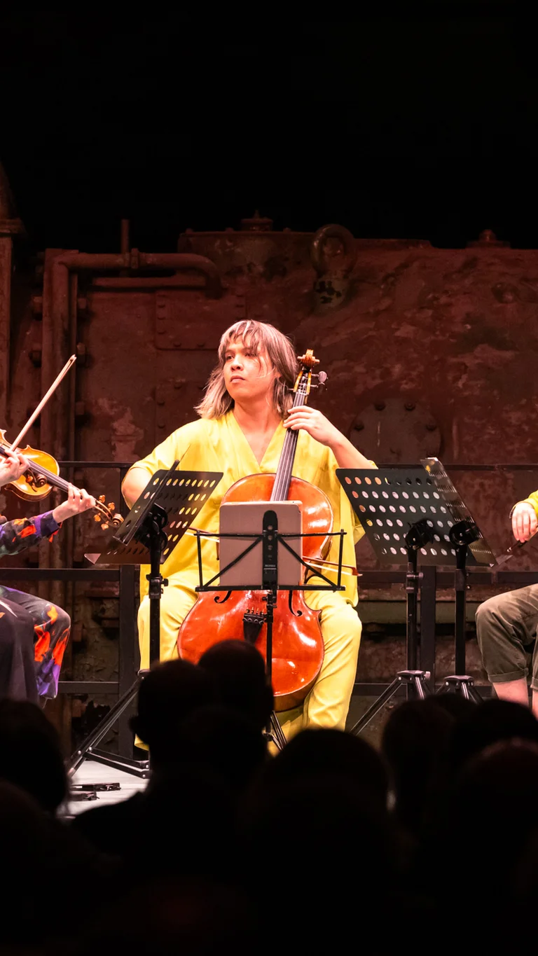Die Musiker:innen des Attacca Quartet gemeinsam mit Caroline Shaw auf der Bühne. Alle sitzen in einem Halbkreis und spielen auf ihren Streichinstrumenten.