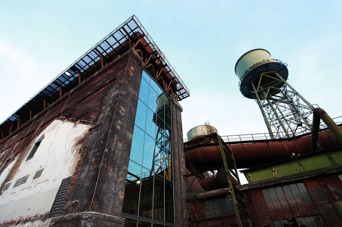 Außenansicht des Dampfgebläsehauses in Bochum, mit industriellen Details wie Rohren und einem Wasserturm, die sich gegen den blauen Himmel abheben.