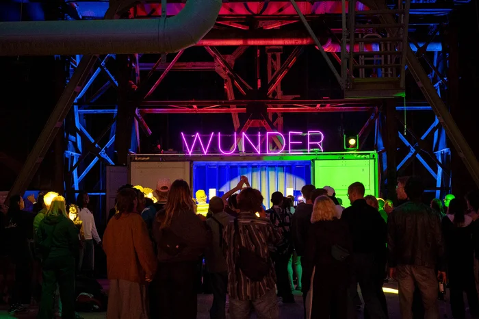 A crowd of visitors celebrates in front of the colourful DJ area with an illuminated WUNDER sign.