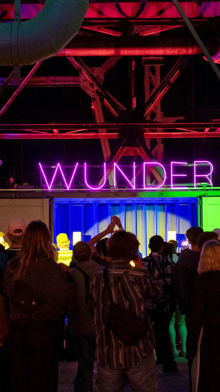 A crowd of visitors celebrates in front of the colourful DJ area with an illuminated WUNDER sign.