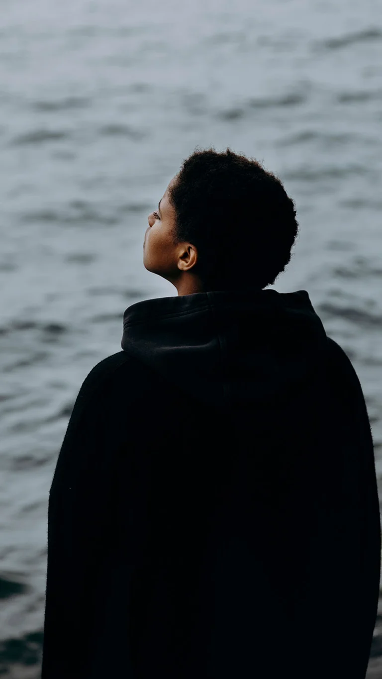 Singer-Songwriterin Meskerem Mees fotografiert von hinten, auf Wasser schauend.