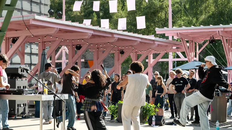 Die Mitglieder von Patina Records unter der rosafarbenen Holzkonstruktion des Festivalzentrums Wunderland; davor Publikum, das die Show verfolgt.