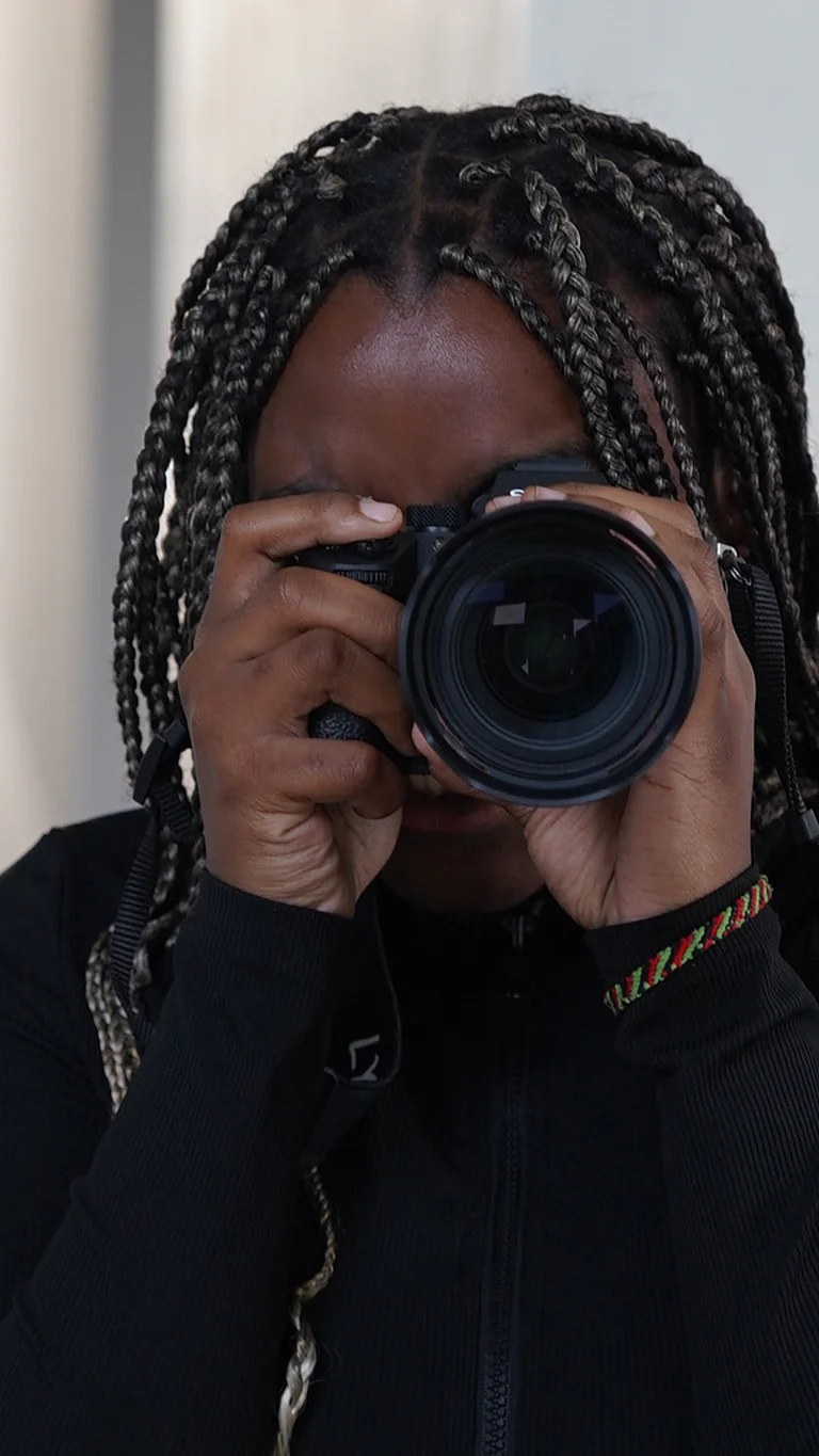 Eine Person in schwarzem Oberteil hält eine Kamera in den Händen und schaut durch den Sucher.