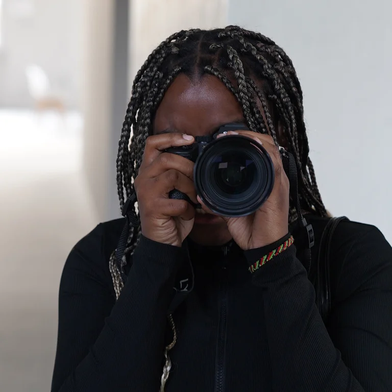 Eine Person in schwarzem Oberteil hält eine Kamera in den Händen und schaut durch den Sucher.