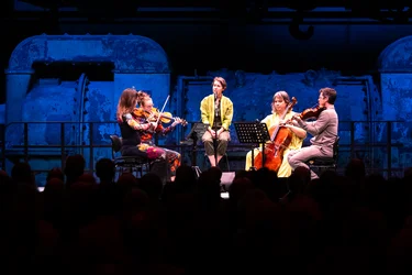 Caroline Shaw singt mit dem Attacca Quartet vor blau beleuchteter Industriekulisse.