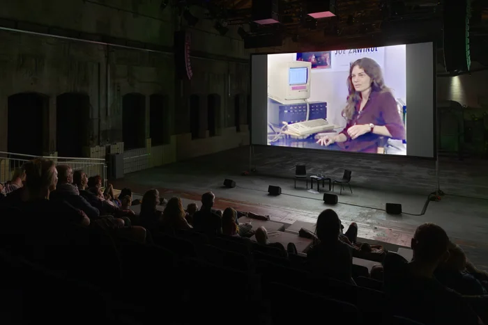 Publikum schaut in einer Industriehalle eine Filmvorführung auf großer Leinwand.