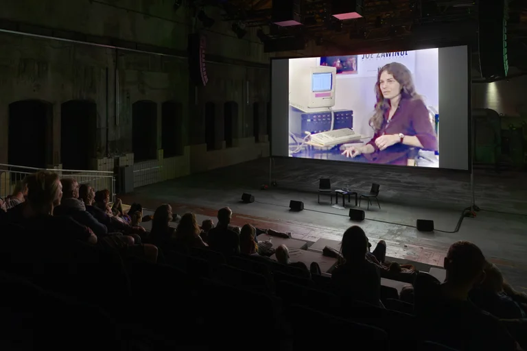 Audience watching a film screening on a large screen inside an industrial hall.