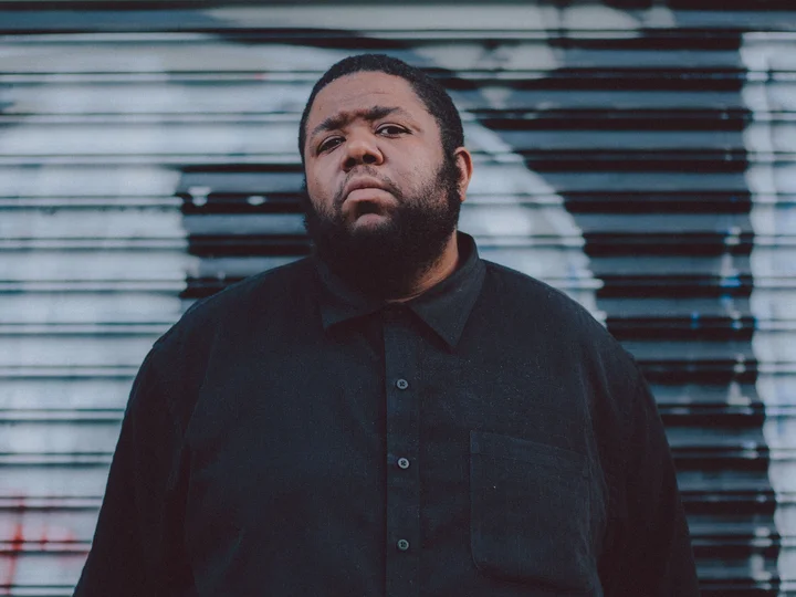 Portrait of Tyshawn Sorey looking into the camera. A garage door painted with graffiti can be seen in the background.