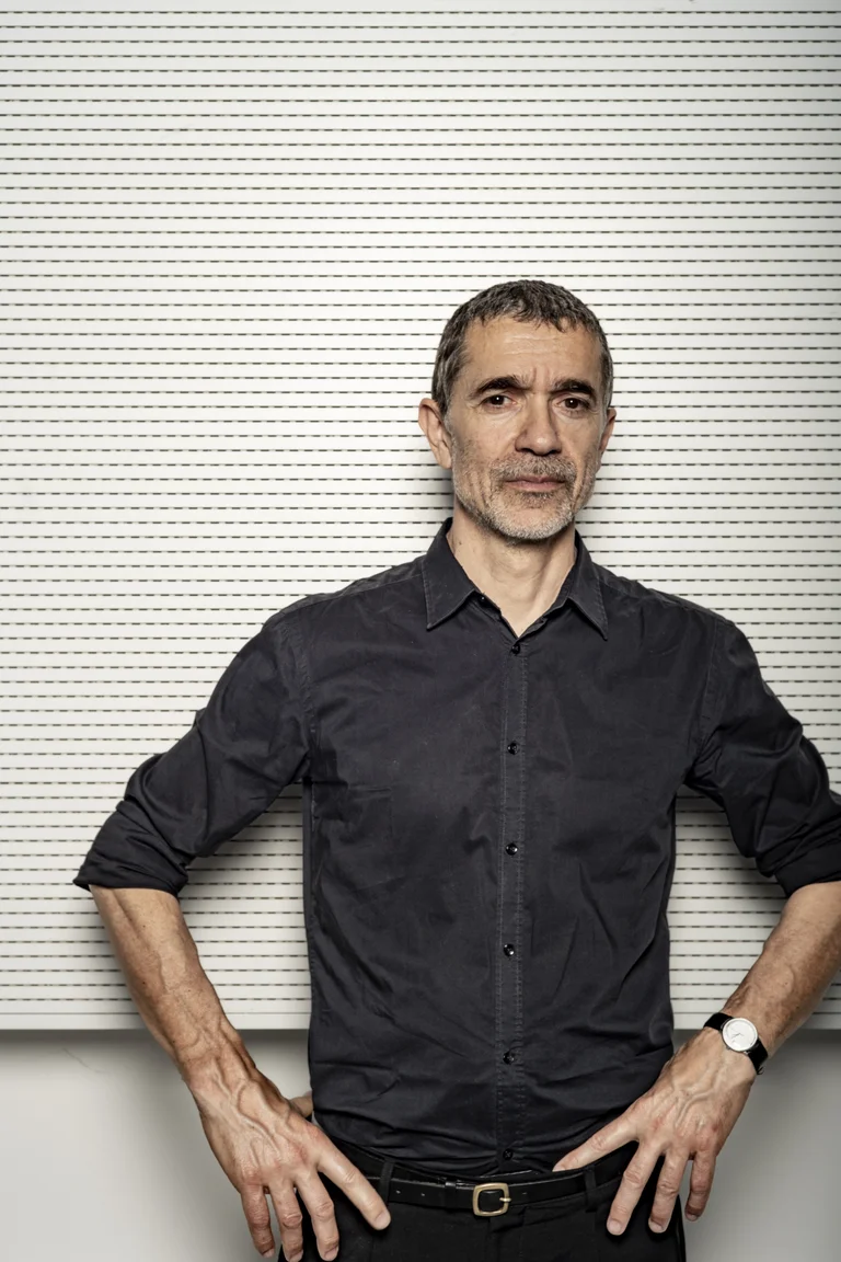 Man in black shirt, the director Romeo Castellucci, posing in front of white wall