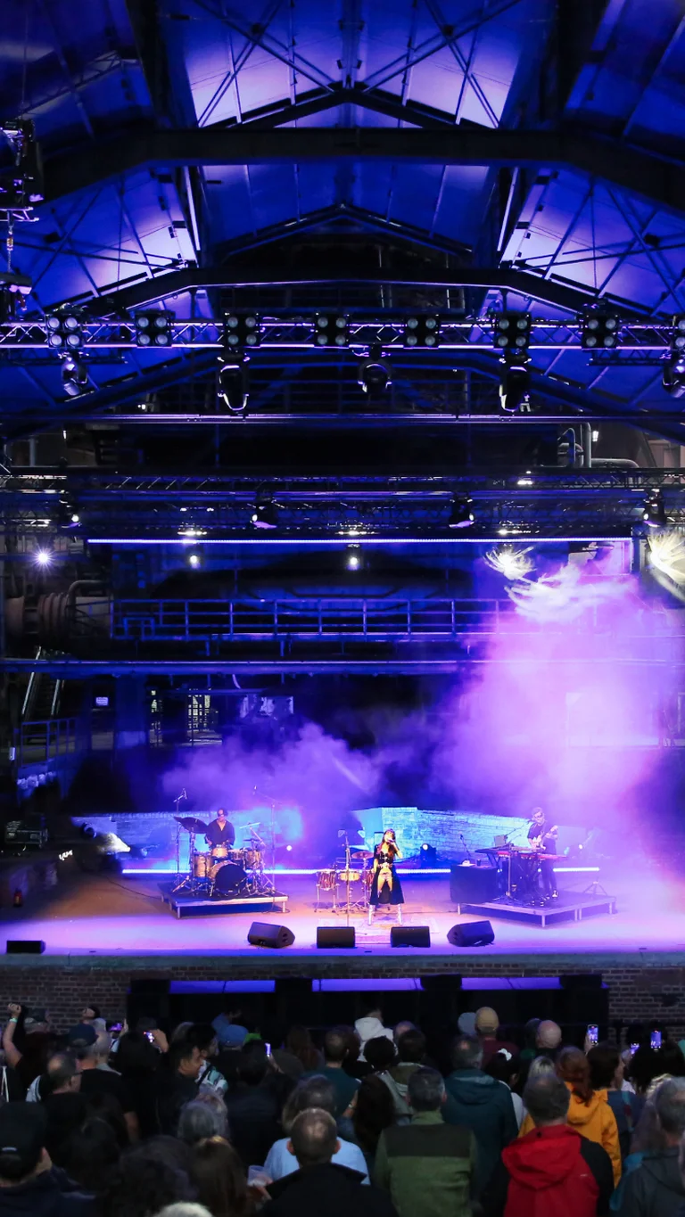 Singer Gaye Su Akyol performing in front of an audience in the Gießhalle, bathed in purple light.