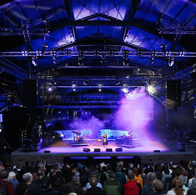 Singer Gaye Su Akyol performing in front of an audience in the Gießhalle, bathed in purple light.
