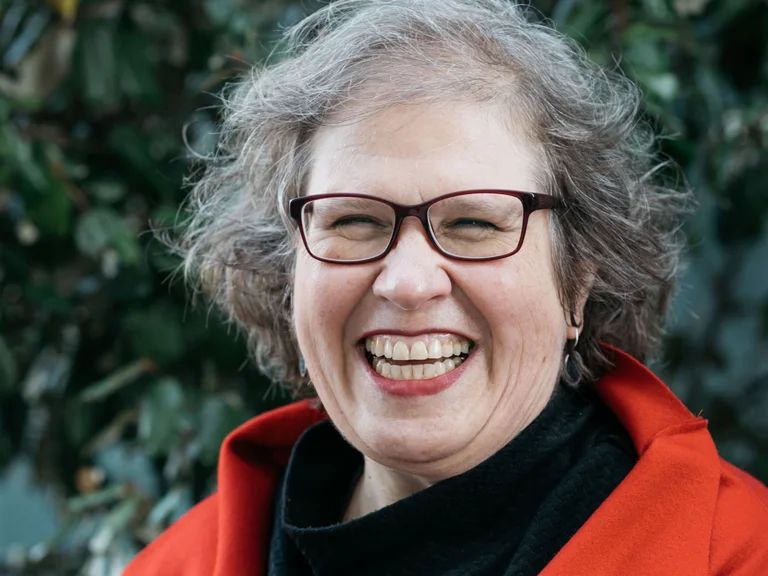 Portrait von Ulrike Czermak in einem roten Mantel, die in die Kamera lächelt