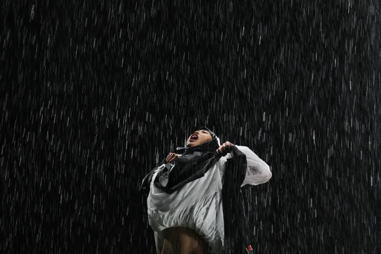Ting Lee standing in heavy rain, looking upward with mouth open.