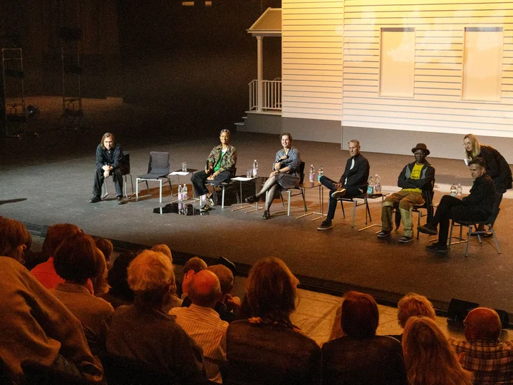 Publikumsgespräch mit Beteiligten der Produktion "I Did It My Way", die vor einer weißen Fassade, dem Bühnenbild, sitzen. Im Vordergrund erkennt man verschwommen Publikum.