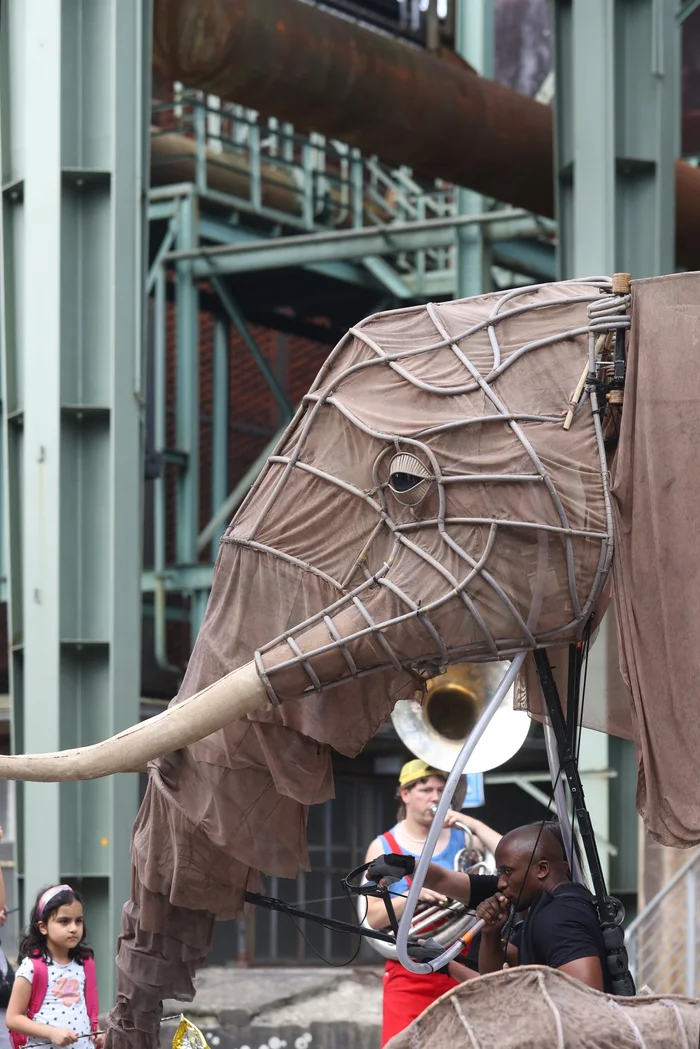 A life-size elephant figure at the ‘Celebration Parade’ in the Duisburg-Nord Landscape Park, with a musician playing a trumpet in the background.