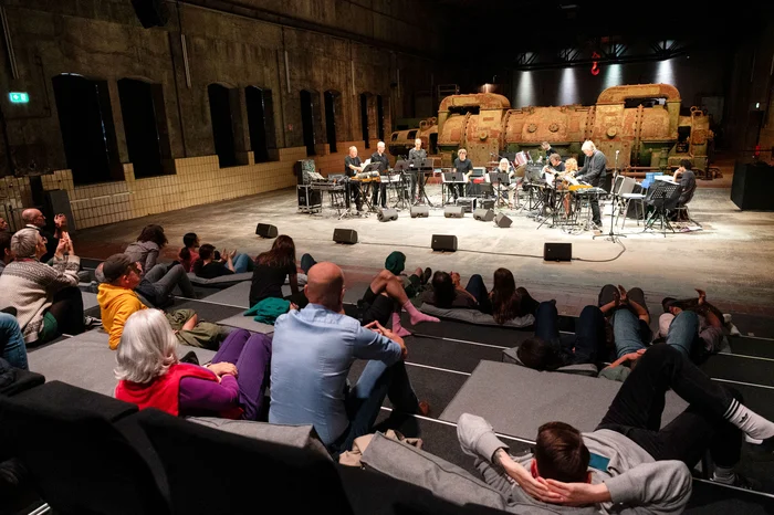 Musicians perform on stage while the audience sits and lies relaxed in front.
