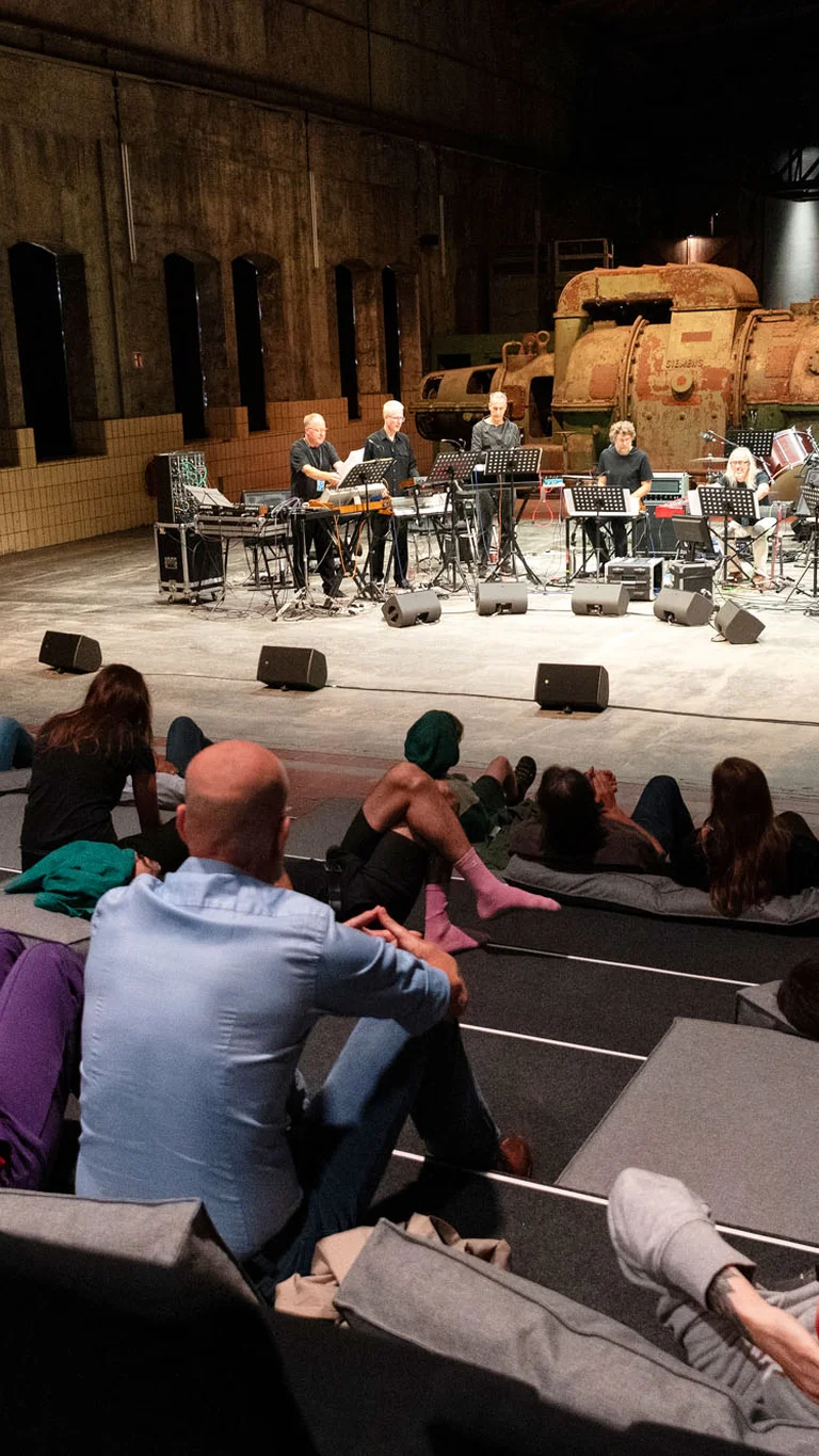 Musicians perform on stage while the audience sits and lies relaxed in front.