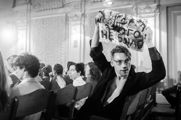 Schwarz-weiß Film still aus dem Film "Leto", auf dem eine Person ein Schild mit kirilkyrillischen Buchstaben hochhält.