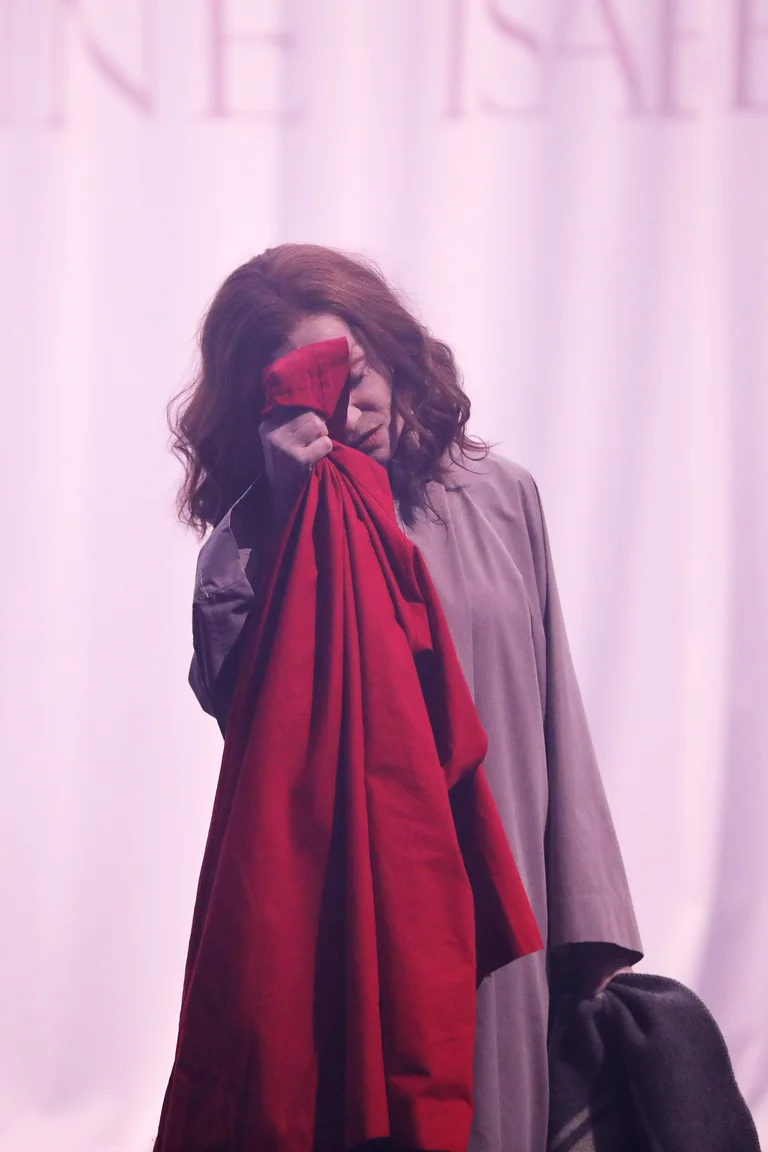 Red-haired woman, the actress Isabelle Huppert, in front of light background with red sheet