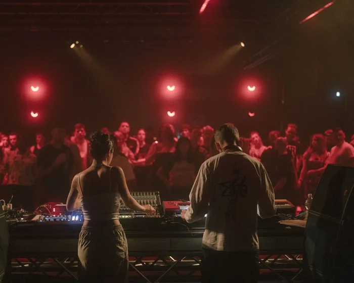 Zwei DJs in rotem Licht vor Publikum