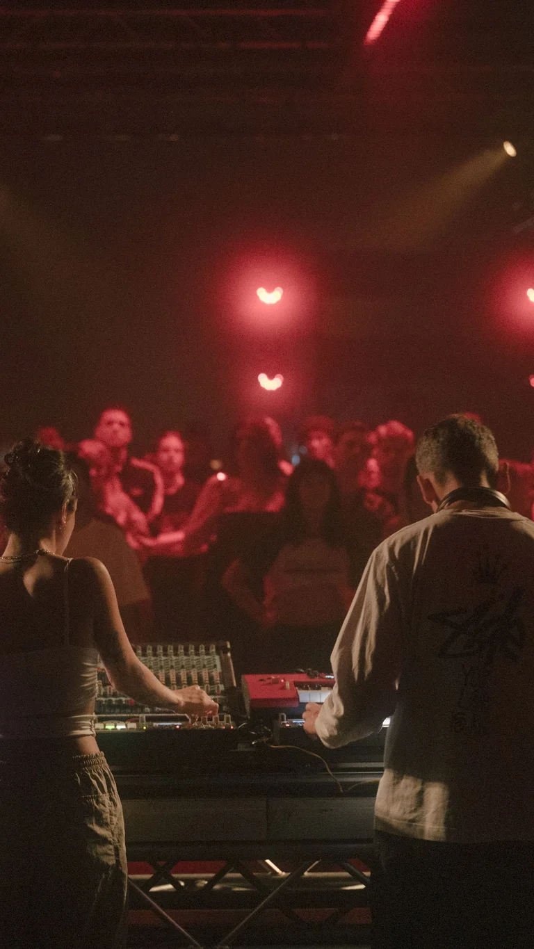 Two DJs in red light in front of an audience