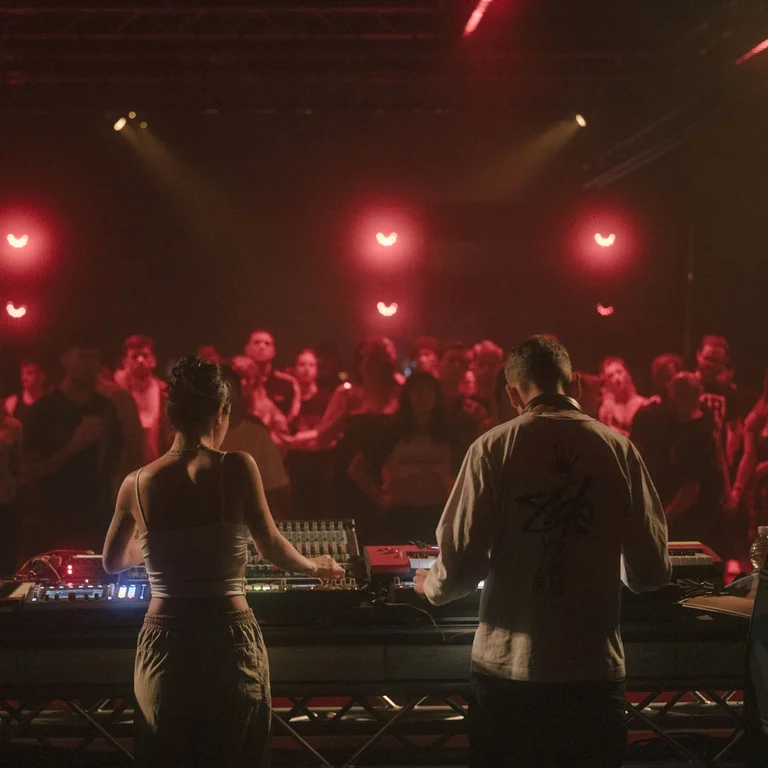 Two DJs in red light in front of an audience