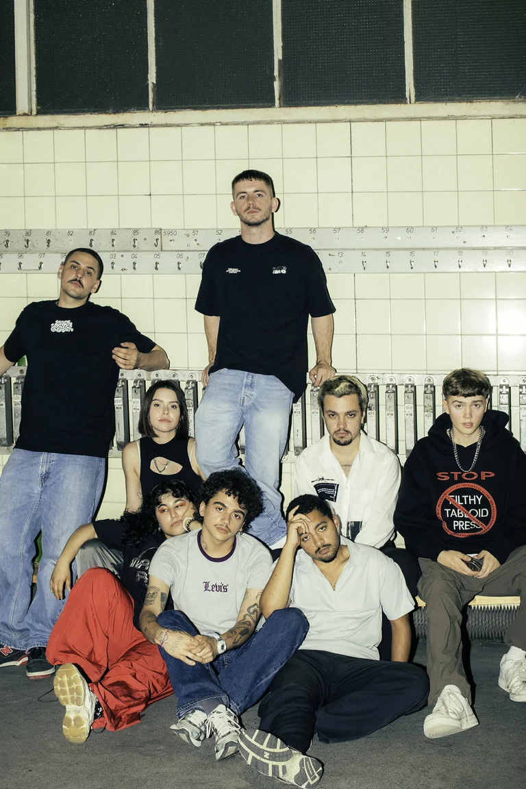 The musicians of Patina Records are standing and sitting in front of a brightly tiled wall. A total of eight people are visible. They are looking into the camera with serious expressions.