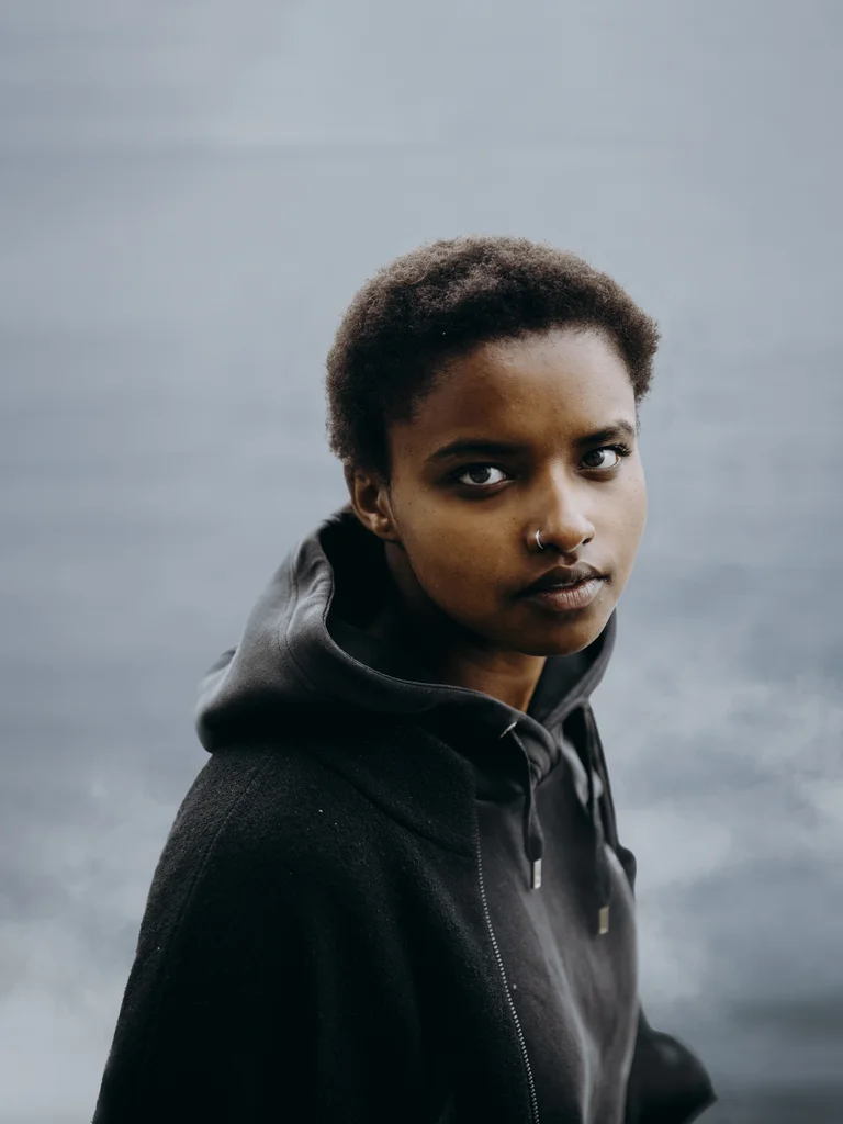 Meskerem Mees trägt einen schwarzen Pullover und schaut direkt in die Kamera. Im Hintergrund ist Wasser zu sehen.