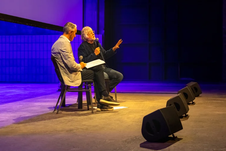 Ivo Van Hove and Will Gregory sitting on stage and speaking with microphones.