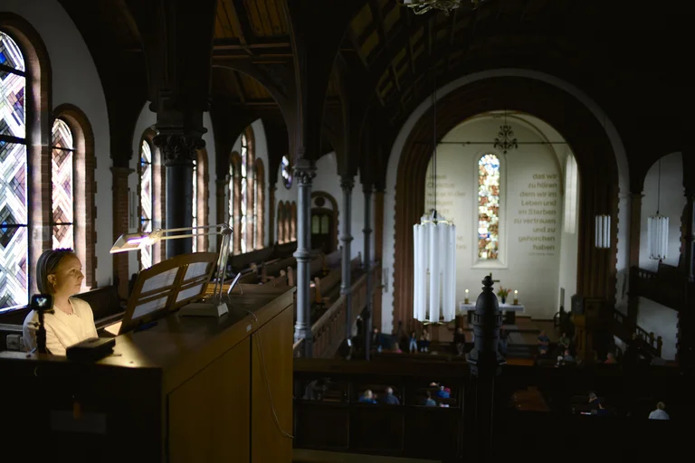 Pianist and organist Eliza McCarthy at the organ in the Evangelical Church at the Market in Katernberg during the event 124 Years of Reverb. Seen from the gallery, the perspective opens onto the church interior with its stained-glass windows, high wooden ceilings, and altar space, while McCarthy sits focused at the organ console.