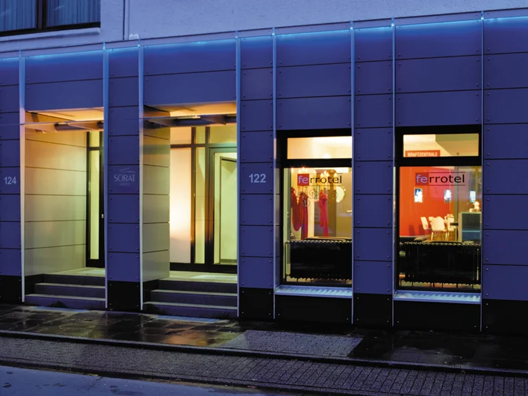Night view of the entrance area of ferrotel Duisburg, with illuminated windows and a modern façade design.