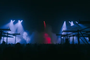 Eine große Menschenmenge feiert in der Jahrhunderthalle Bochum mit Lichtstrahlen, Nebel und Gerüststruktur.