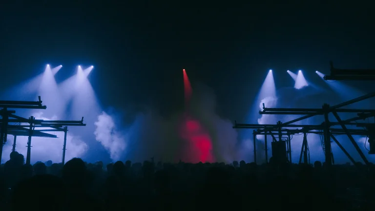 A large crowd celebrates in the Jahrhunderthalle Bochum filled with spotlights, fog, and scaffold structures.