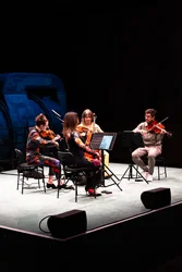 Das Attacca Quartet spielt auf einer hellen Bühne vor dunkler Industriekulisse.
