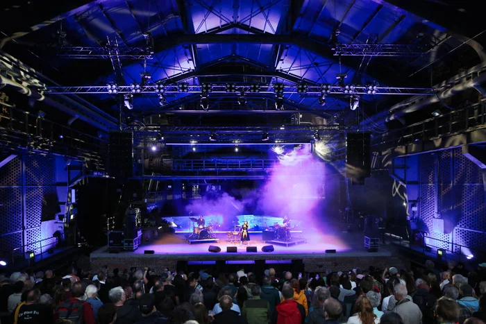 View inside a large hall with a stage where Gaye Su Akyol and her band perform in purple light and haze in front of a large audience.