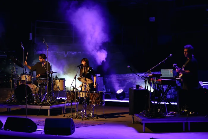 Gaye Su Akyol performs with her band on stage in purple light and haze.