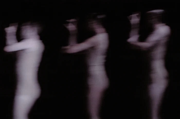 Blurred silhouettes of three human figures move against a dark background. The motion blur evokes dynamism, transience, and a ghostly atmosphere.