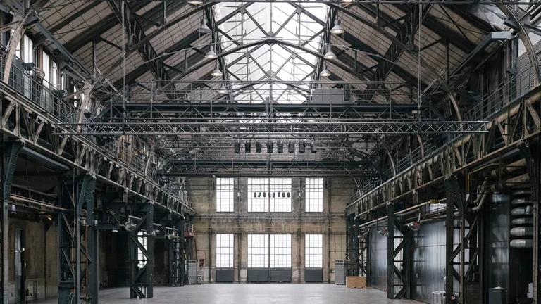 View of the interior of the Jahrhunderthalle Bochum, featuring its expansive space, high steel beams, and large windows letting in natural light. The hall appears both open and industrial.