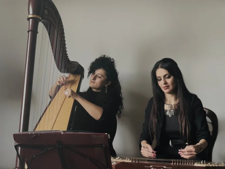The musicians Zainab and Areezo dressed in black play on the harp / on the santur, against a neutral background.