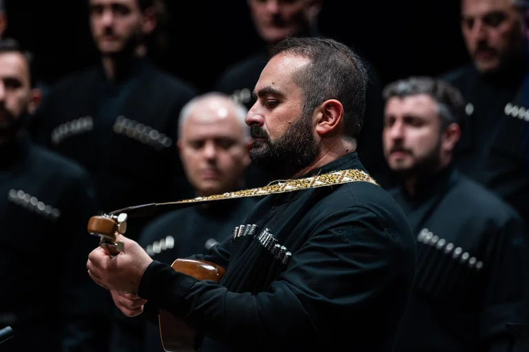 Musiker und ein Chor stehen zusammen auf einer Bühne und musizieren.