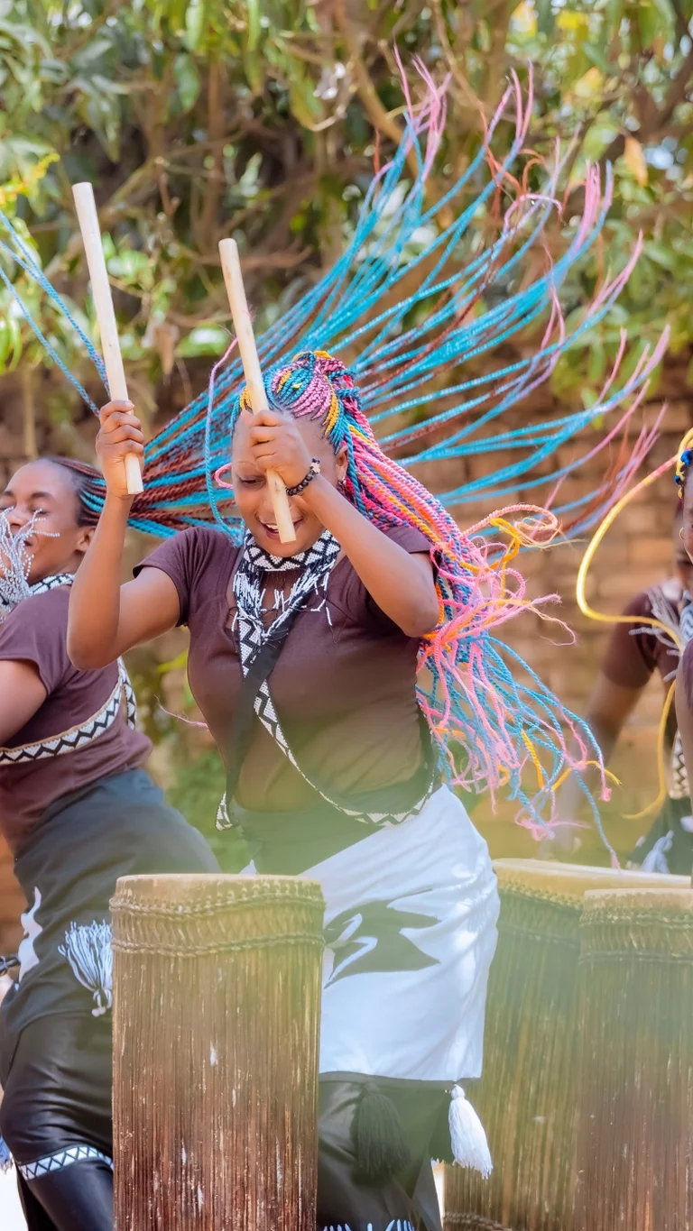 Drei Trommlerinnen schlagen auf ihre Instrumente, während Bewegung, Rhythmus und Gruppendynamik die Szene prägen.