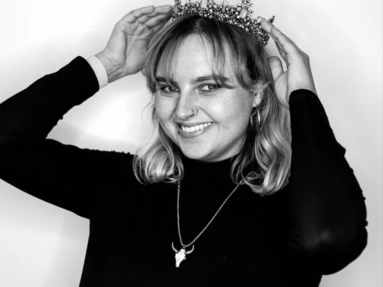 Kassandra Widera lächelt in die Kamera und setzt sich eine verzierte Krone auf, aufgenommen vor hellem Hintergrund