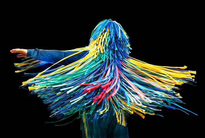 A person is surrounded by colorful, ribbon-like fringes that spread wide during a spin.